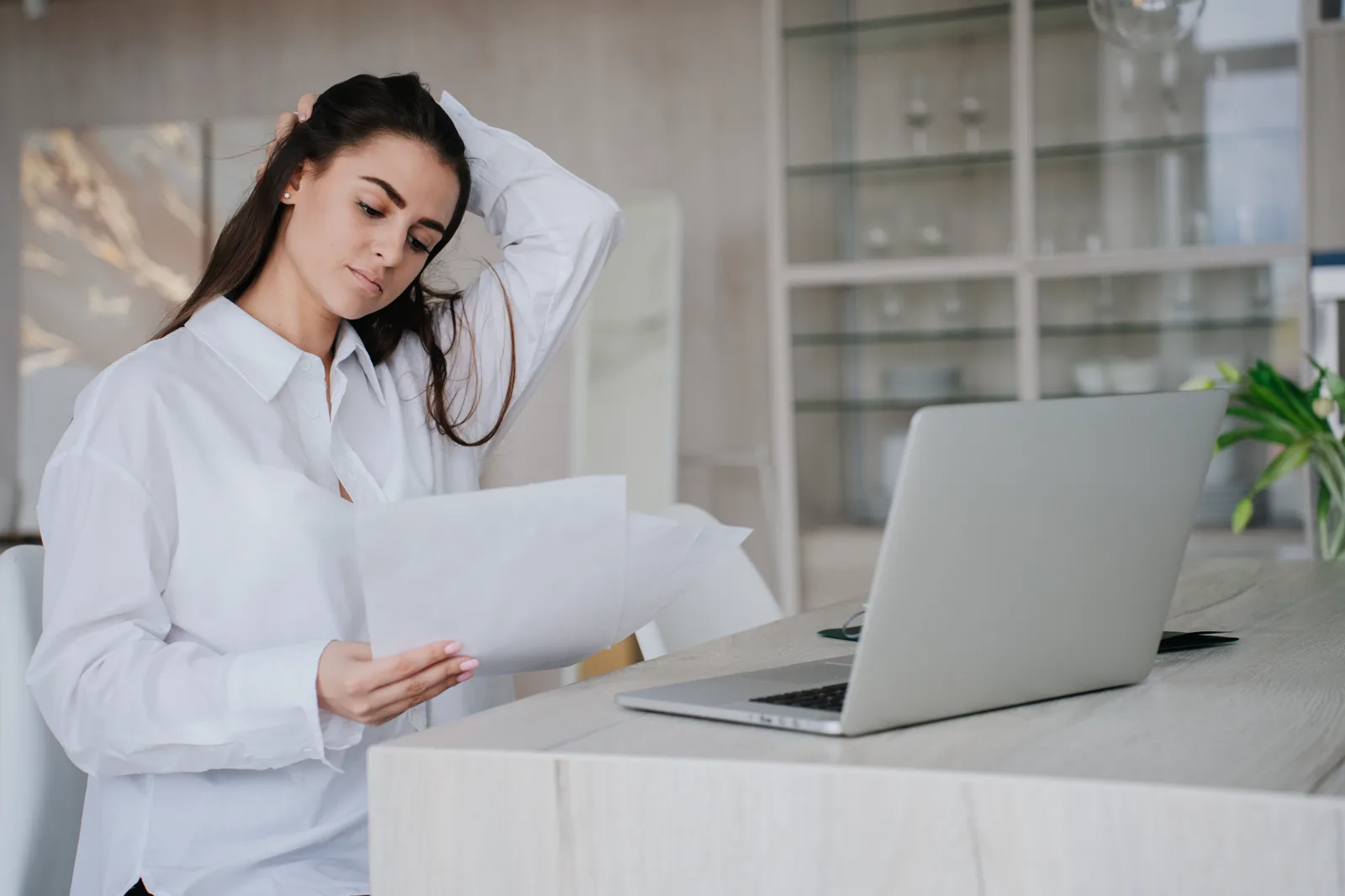 Concerned woman reviewing paperwork beside a laptop at home