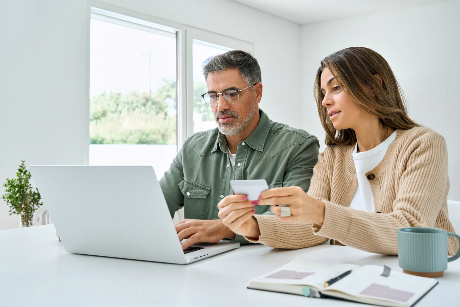 A couple using a laptop and reviewing a card together at home