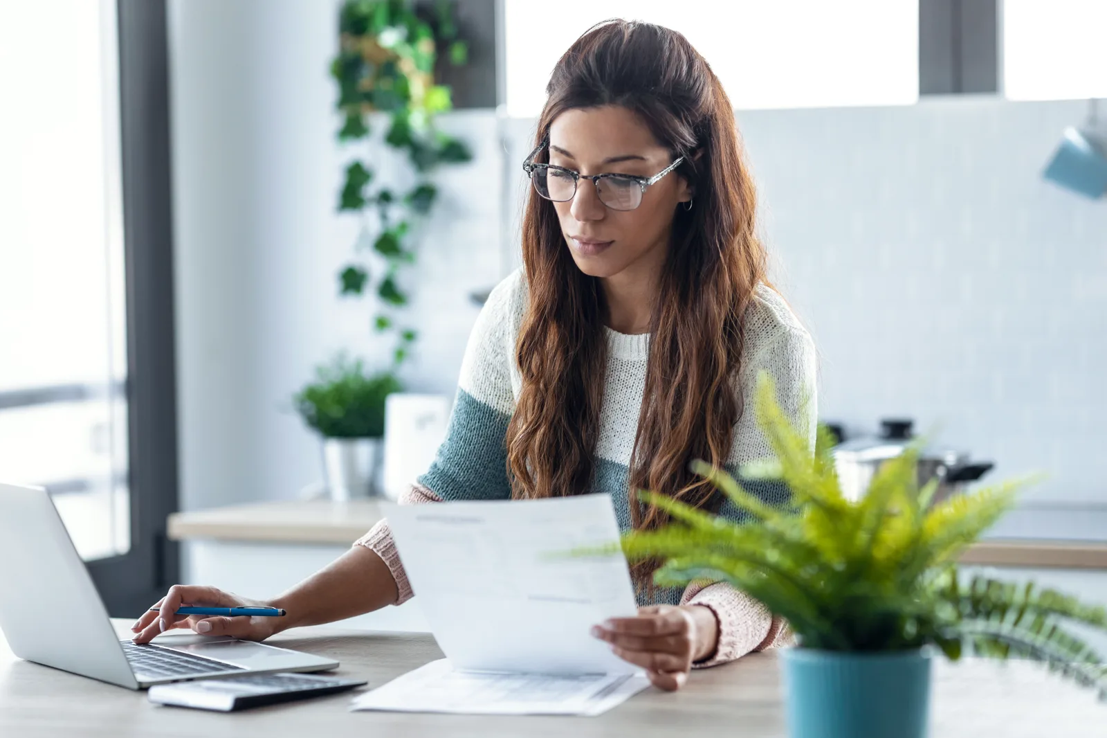 Woman reviewing a benefits document while working on a laptop at home